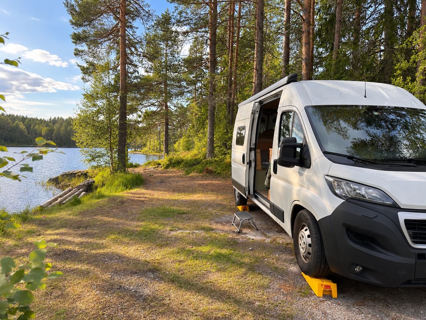 Campervan parked by a quiet forest lake with the sliding door open